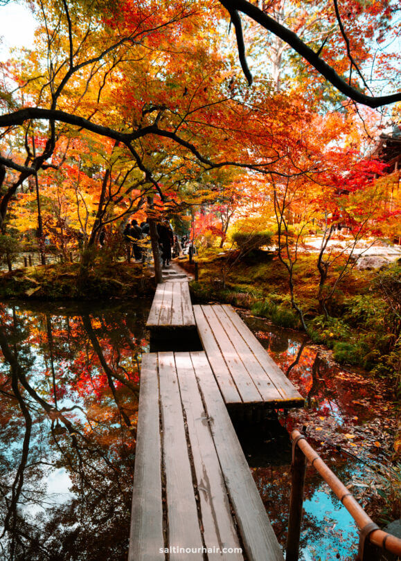 A wooden footbridge crosses a calm pond at Nanzen-ji Temple, surrounded by vibrant autumn foliage in shades of red, orange, and yellow—capturing the serene beauty of autumn in Japan.