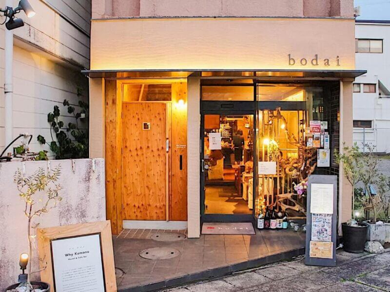 Street view of the entrance to a restaurant named bodai in Nachikatsuura, featuring a wooden door, glass windows, and a warmly lit interior reminiscent of Kumano's welcoming charm.