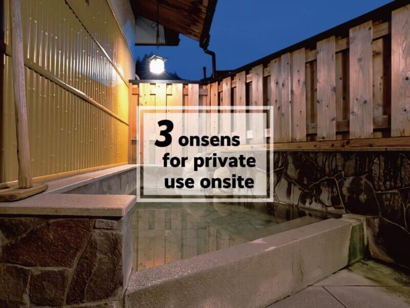 Outdoor onsen area at night with wooden fencing, stone tiles, and a sign that reads 3 onsens for private use onsite at Yunomine Guesthouse—a cozy J-Hoppers guesthouse retreat.