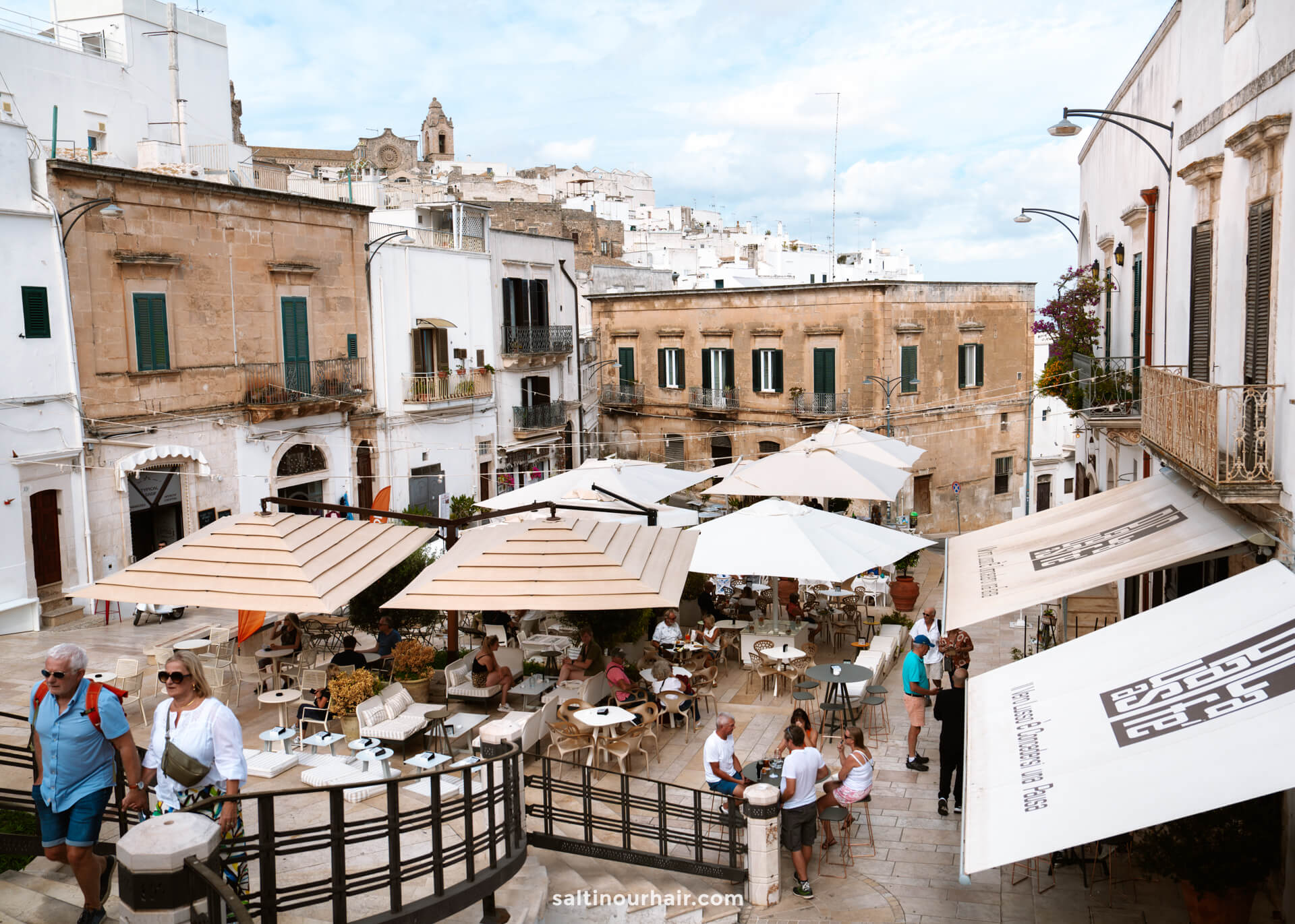 Outdoor café with tables and umbrellas in Pizza Da Libertà, surrounded by old stone buildings in Ostuni, italy