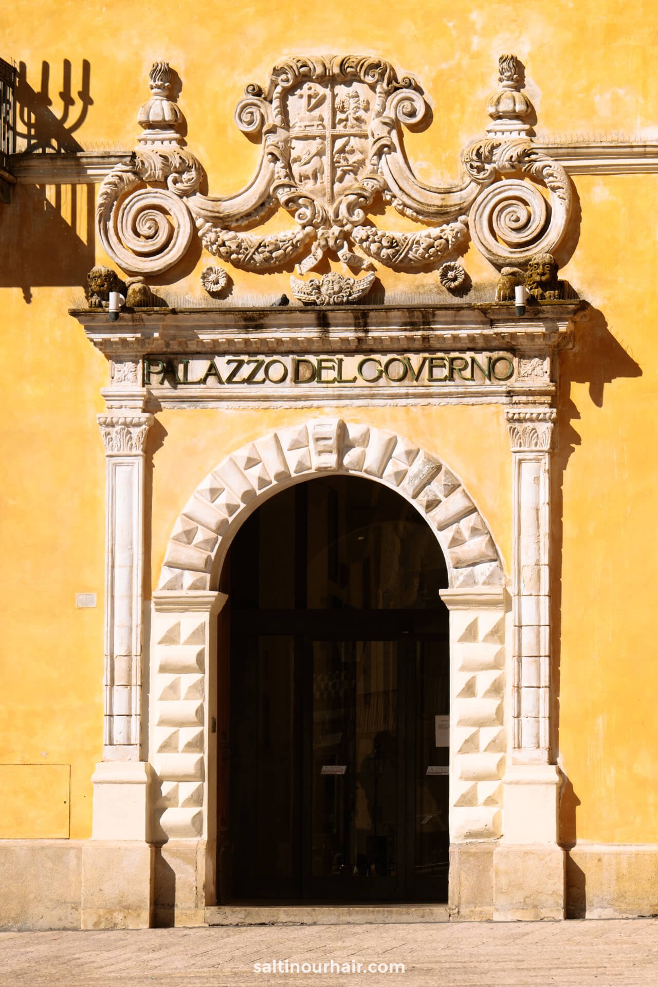 Historic building entrance with ornate stone arch and decorative carvings above, labeled Palazzo del Governo on a yellow facade