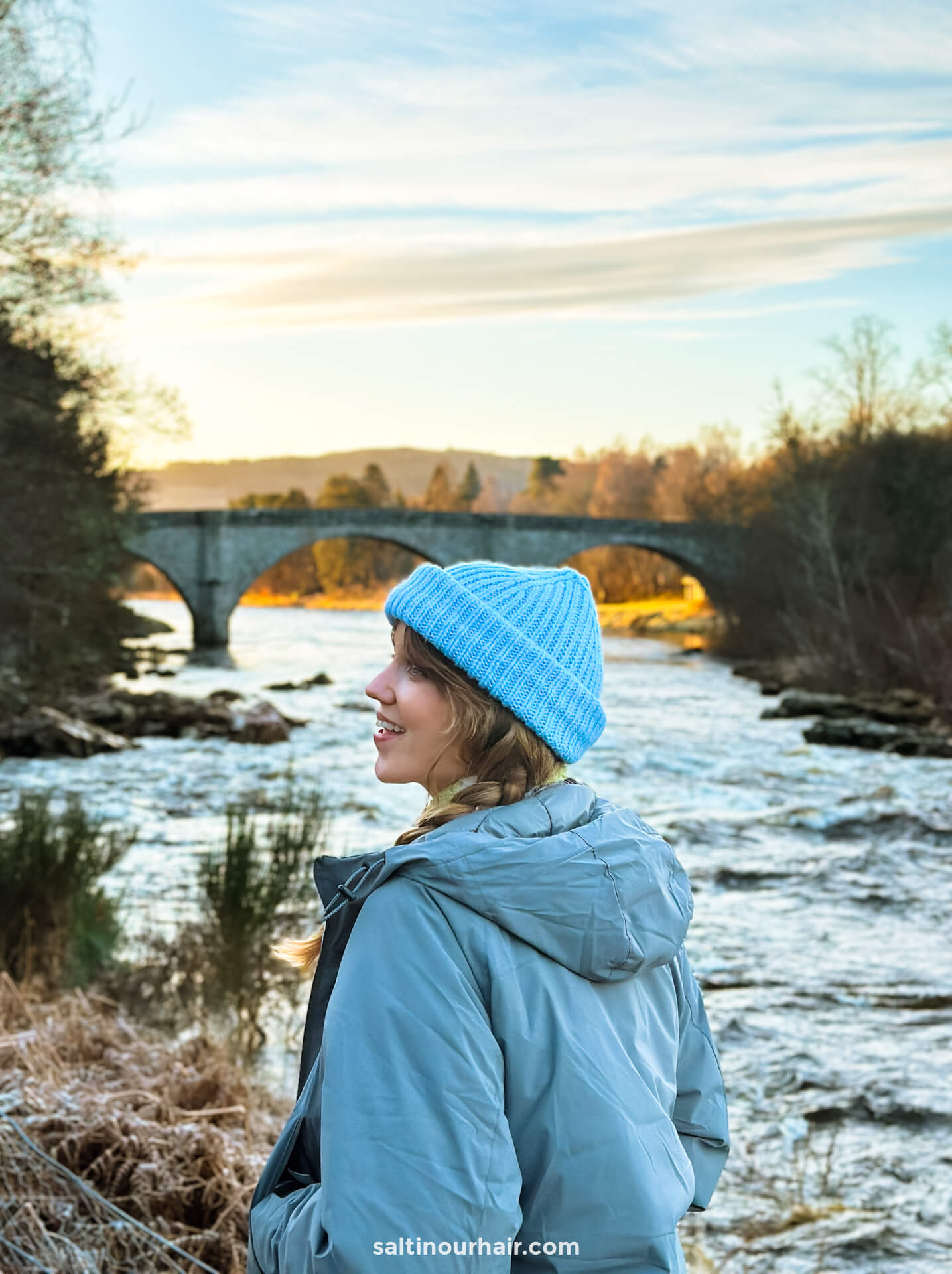 woman with blue beanie enjoying scottish countryside river and bridge