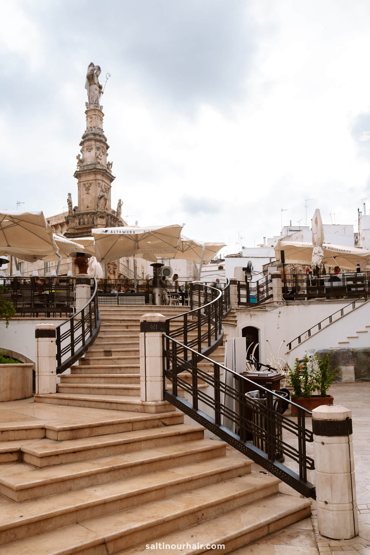Piazza della Libertà in the white city of Ostuni, puglia italy; a tall ornate statue stands in the background.