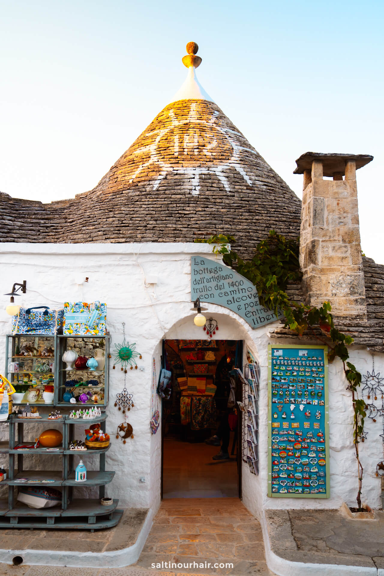 A white stone trullo house with a conical roof in Alberobello, puglia Italy, decorated with souvenirs and magnets at the entrance. 