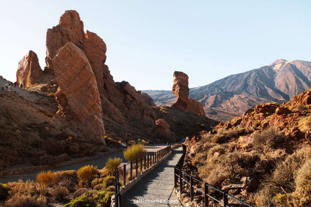 Roques de Garcia Hike, a paved path with railings winds through rocky formations and dry vegetation in Teide National Park, with mount teide in the background