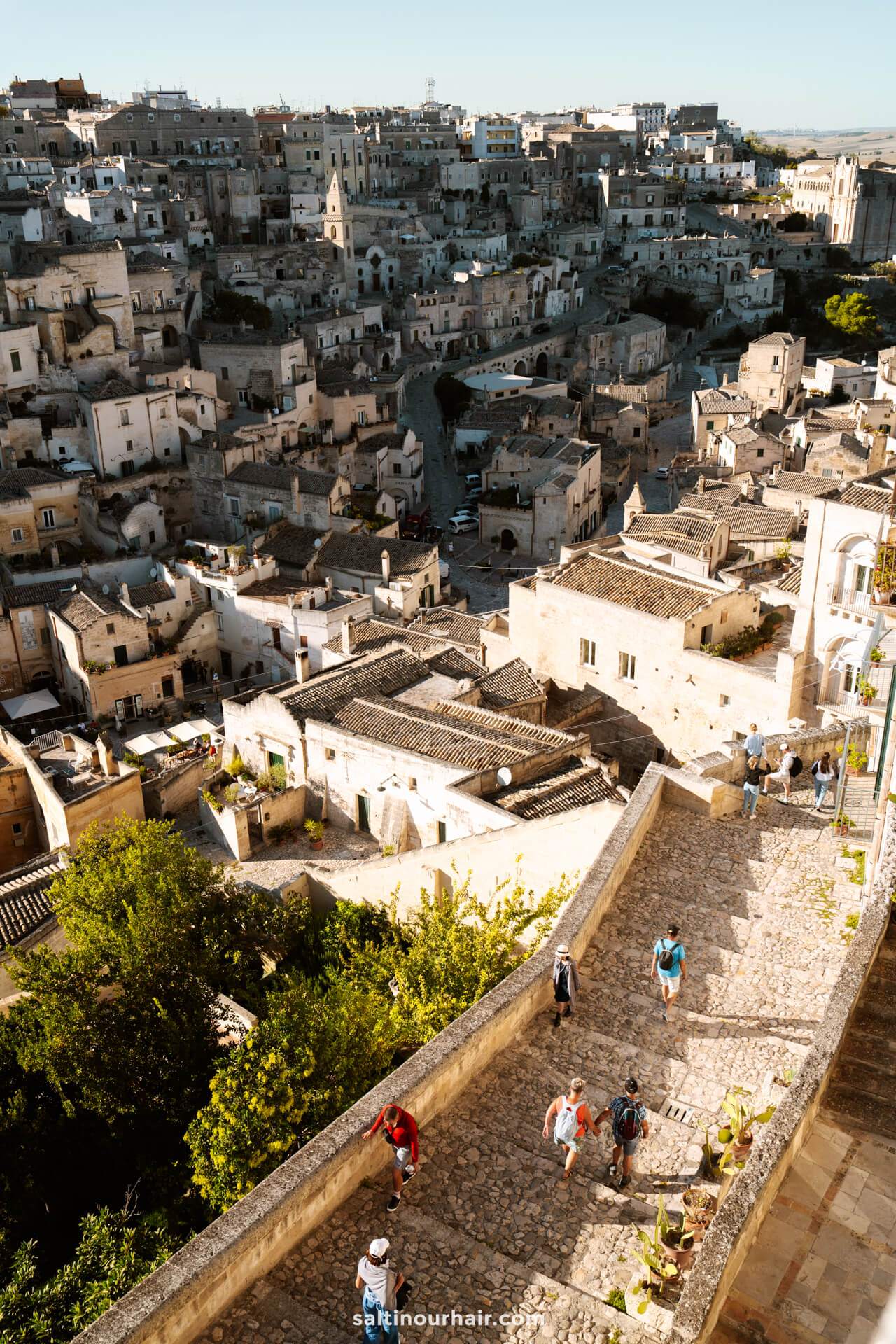 A stone staircase with people walking leads down to a historic cityscape of tightly packed, beige buildings in Matera, Italy