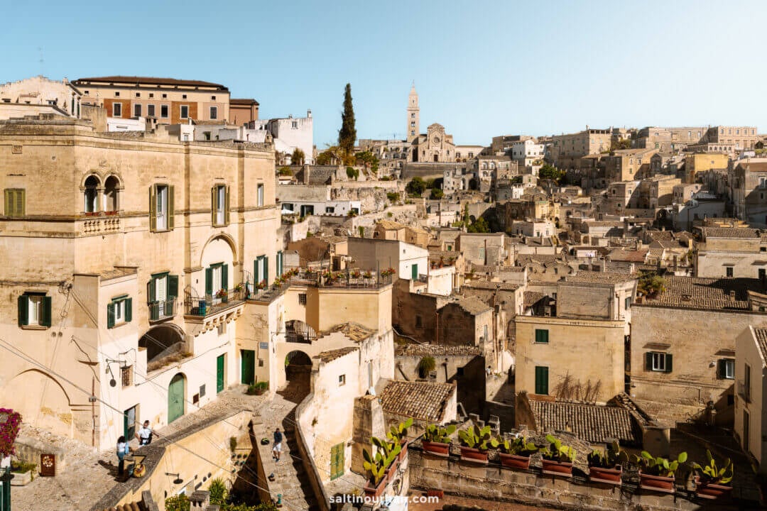 View of historic stone buildings and narrow streets in Matera, Italy, with terraces and balconies visible in the foreground near Belvedere di Piazza Giovanni Pascoli.