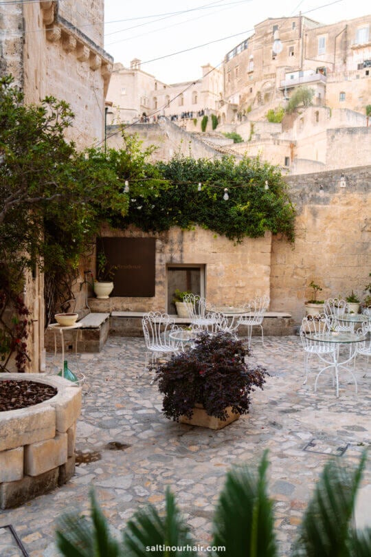 Outdoor courtyard with white metal tables and chairs, set against an old town backdrop in Matera, Italy - best restaurants in Matera