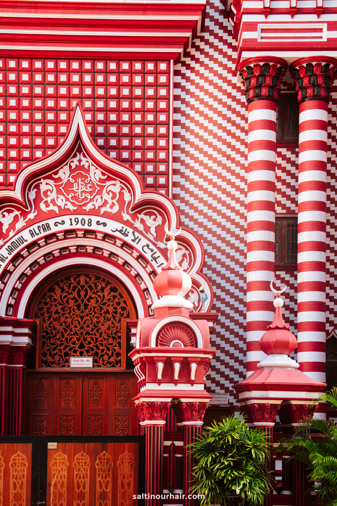 Red and white patterned facade of Jami Ul-Alfar Mosque with arched entrance, columns, and ornate architectural details&mdash;a must-see among things to do Colombo.