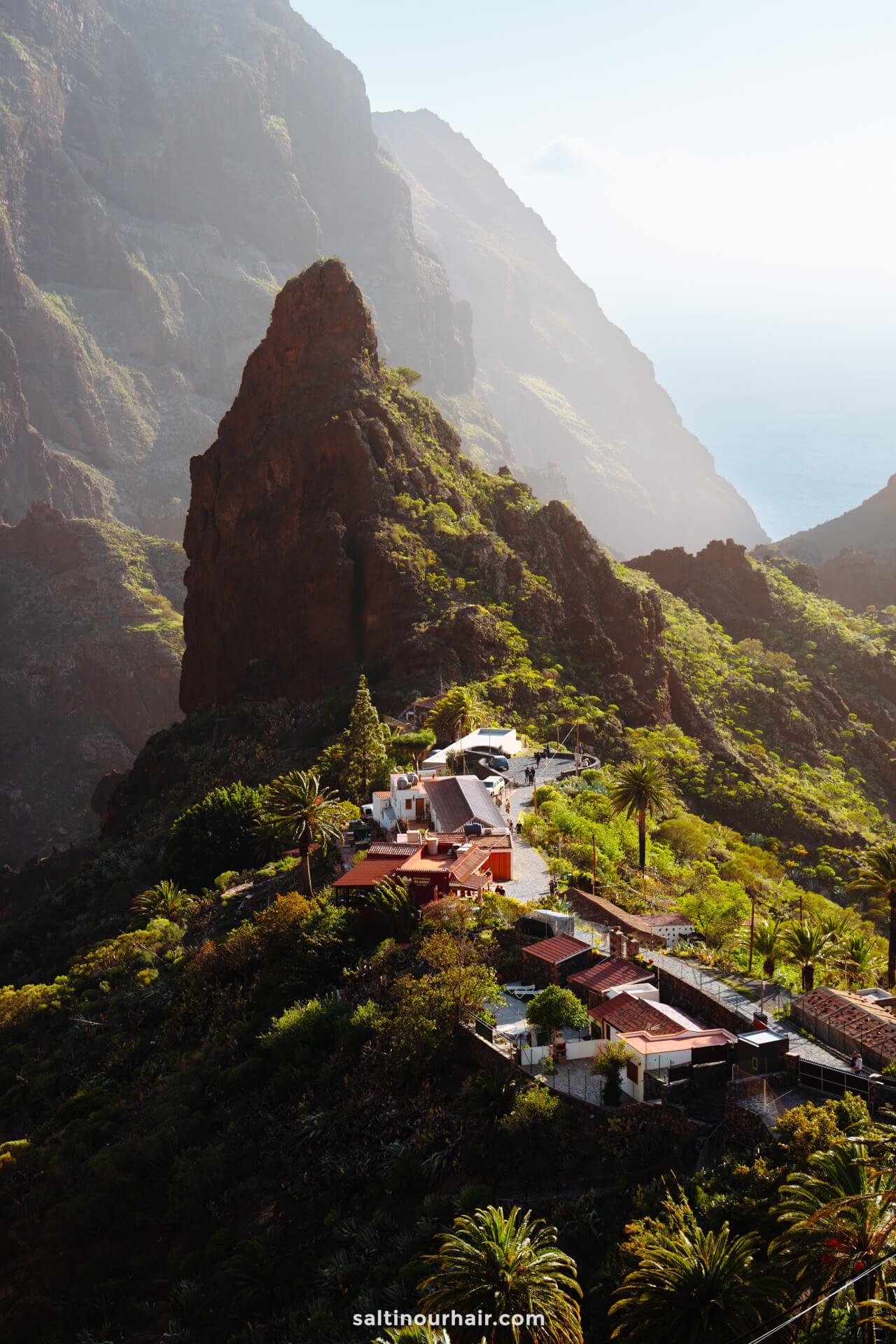 Charming small village with red-roofed houses nestled among lush green mountains, a rocky peak, and the ocean in the distanceâ€”Masca Tenerife offers breathtaking views and serene natural beauty.
