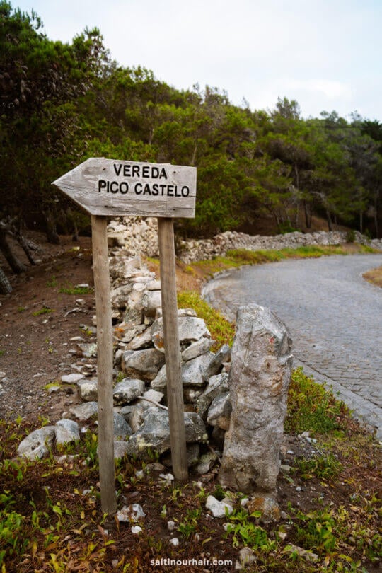 A wooden signpost reads Vereda Pico Castelo and points left, standing beside a cobblestone path with trees and rocks in the backgroundâ€”an inviting start to one of the top things to do in Porto Santo.