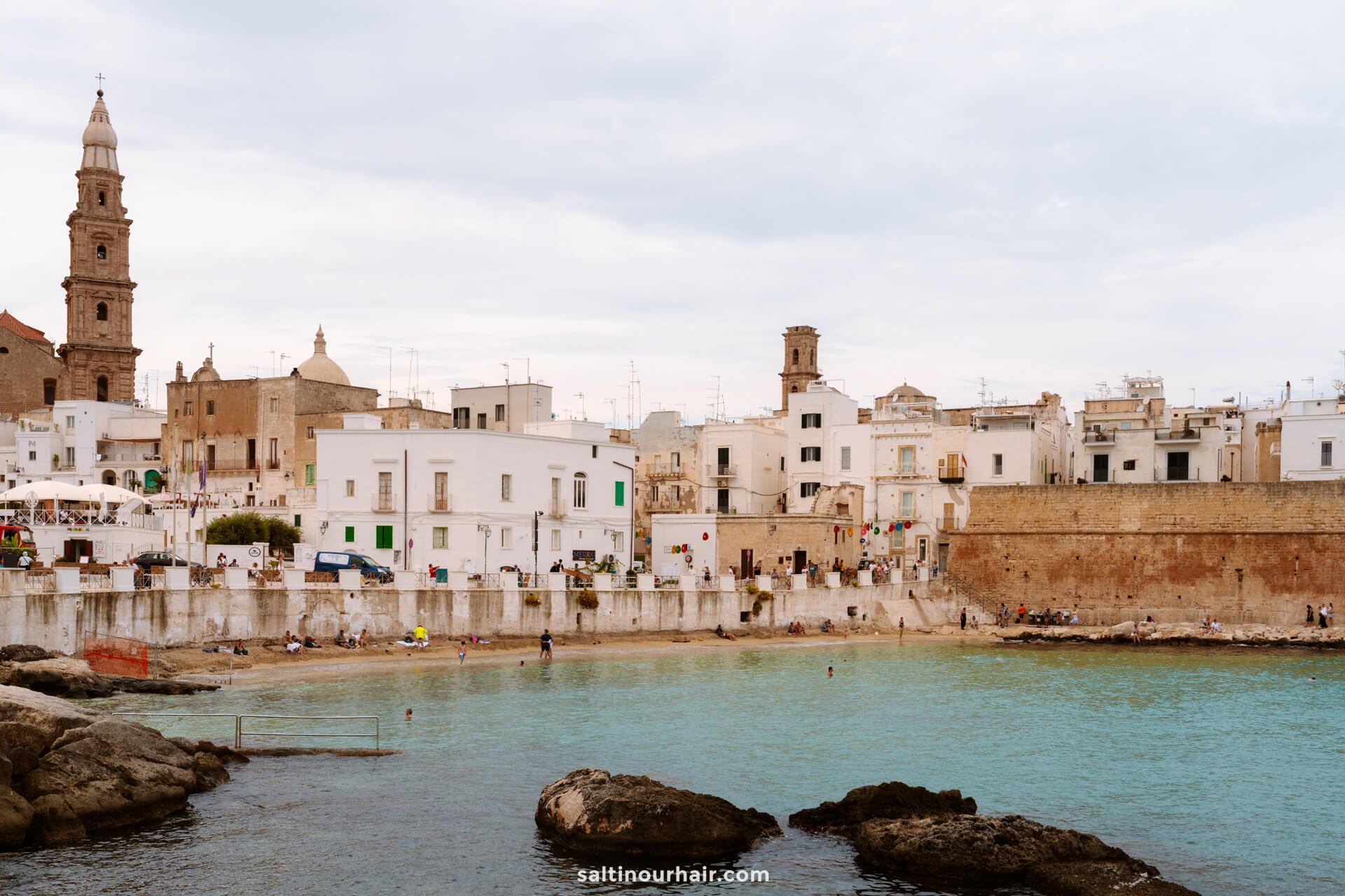 Coastal town of Monopoli, Italy, with white buildings, historic church towers, and a stone seawall