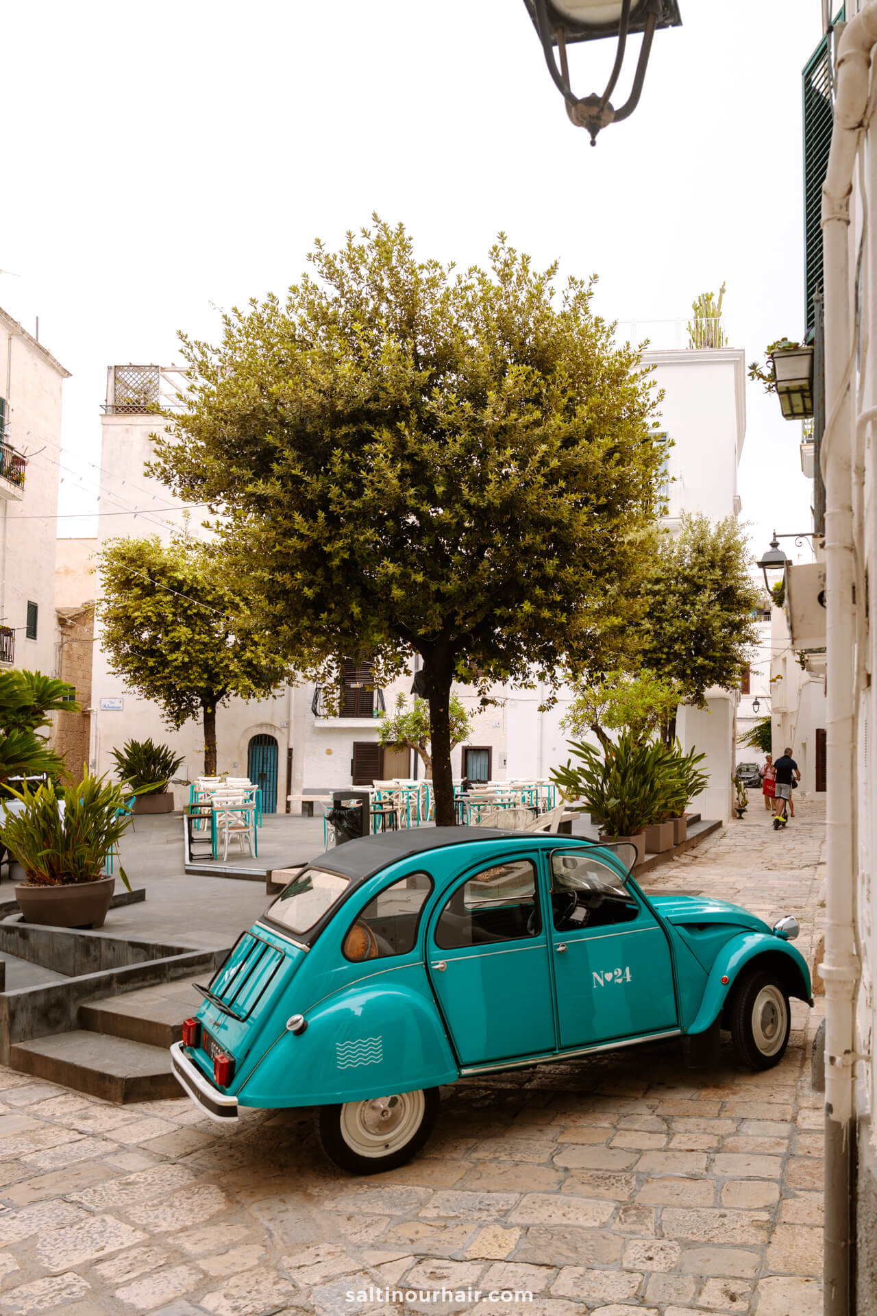 A turquoise vintage car is parked on a cobblestone street in monopoli puglia italy
