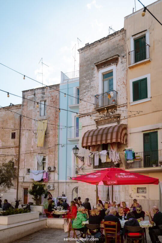 People are dining at outdoor tables in Bari puglia italy, surrounded by old buildings with laundry hanging from balconies