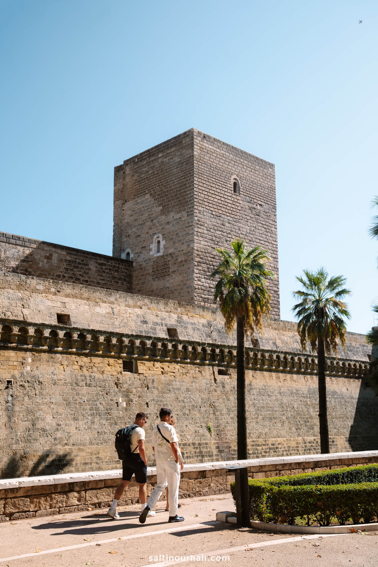 Two people walk along a path in front of Castello Svevo di Bari, one of the top things to do in Bari puglia italy