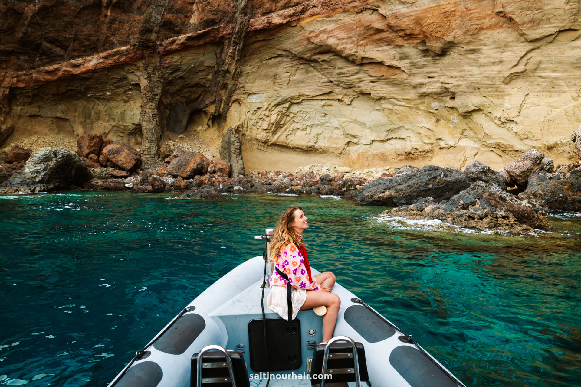 A woman sits at the front of an inflatable boat near rocky cliffs and clear turquoise water, enjoying one of the top things to do in Porto Santo.