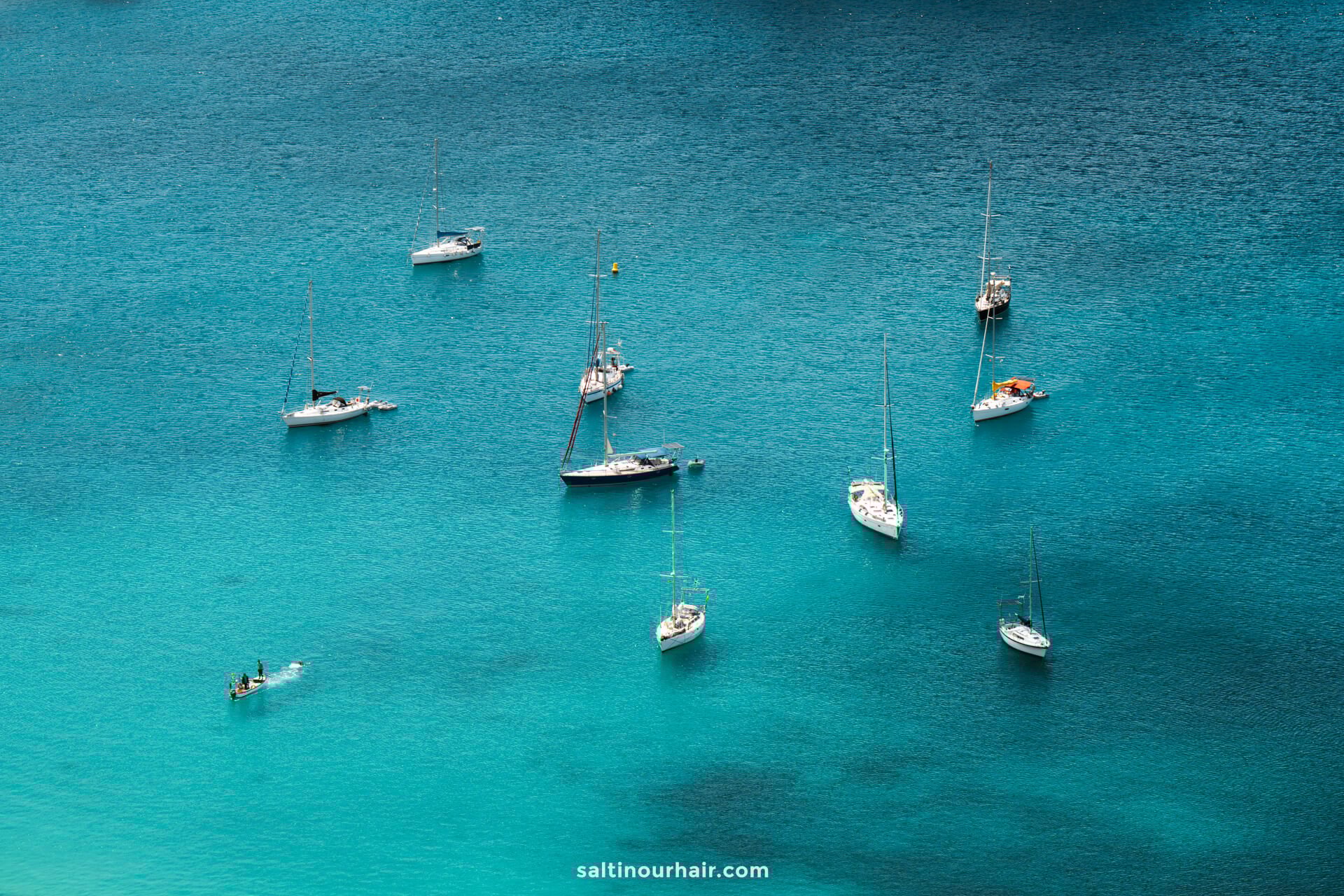 Aerial view of several sailboats and a small kayak floating on calm, clear turquoise waterâ€”one of the serene things to do in Porto Santo.