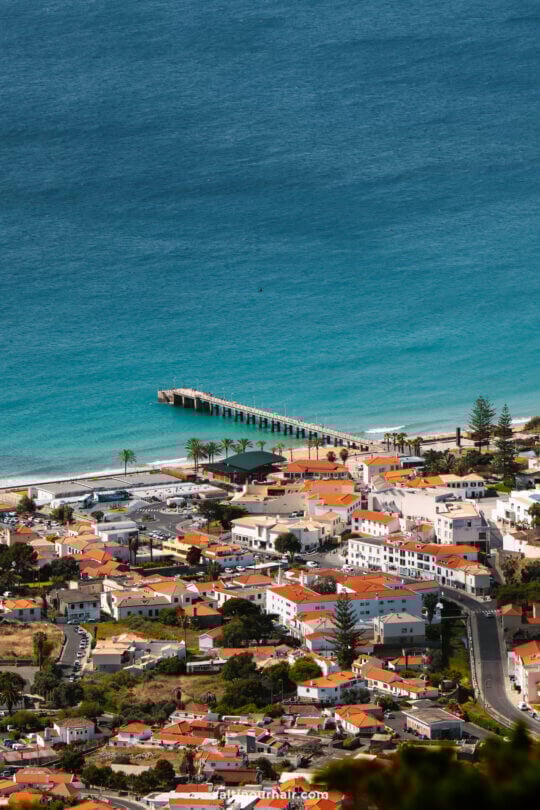 A coastal town in Porto Santo with red-roofed buildings, a sandy beach, and a long pier extending into the turquoise sea