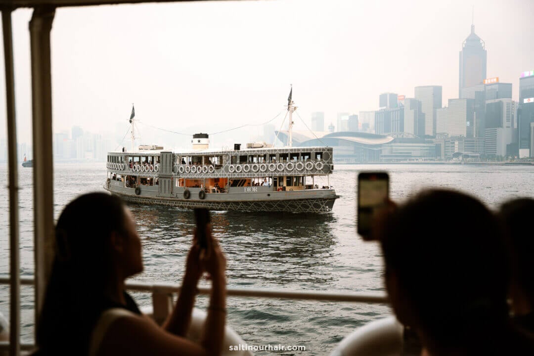 People on a ferry take photos of another ferry gliding across the water, with Hong Kong