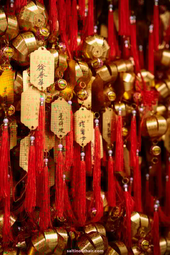 Gold prayer plaques with red tassels hang closely together, displaying handwritten Chinese characters