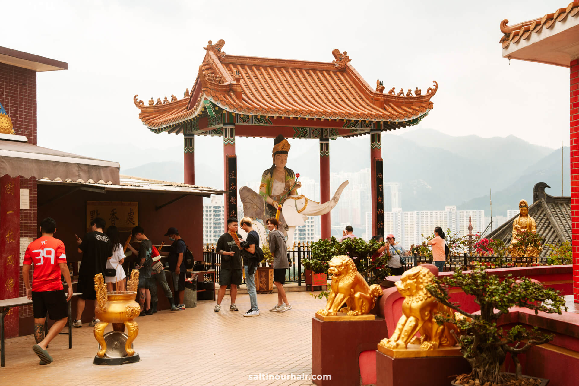 People visit a temple courtyard with a large statue, lion sculptures, and a traditional Chinese pavilion at the 10,000 Buddha Monastery in Hong Kong