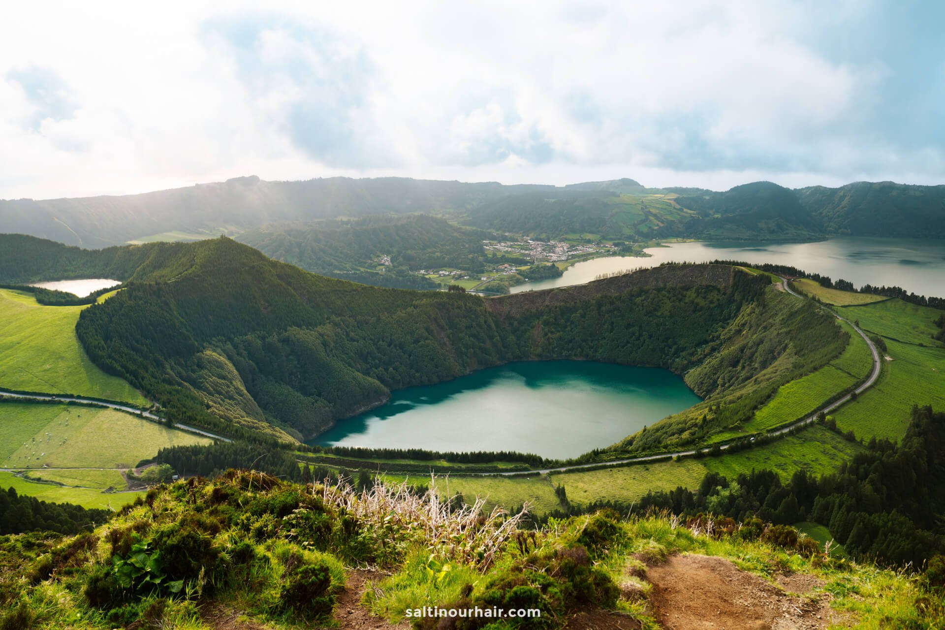 A wide view of Sete Cidades, a twin lake in a volcanic crater surrounded by green hills and a winding roadâ€”one of the must-see things to do in SÃ£o Miguel, Azores, Portugal.