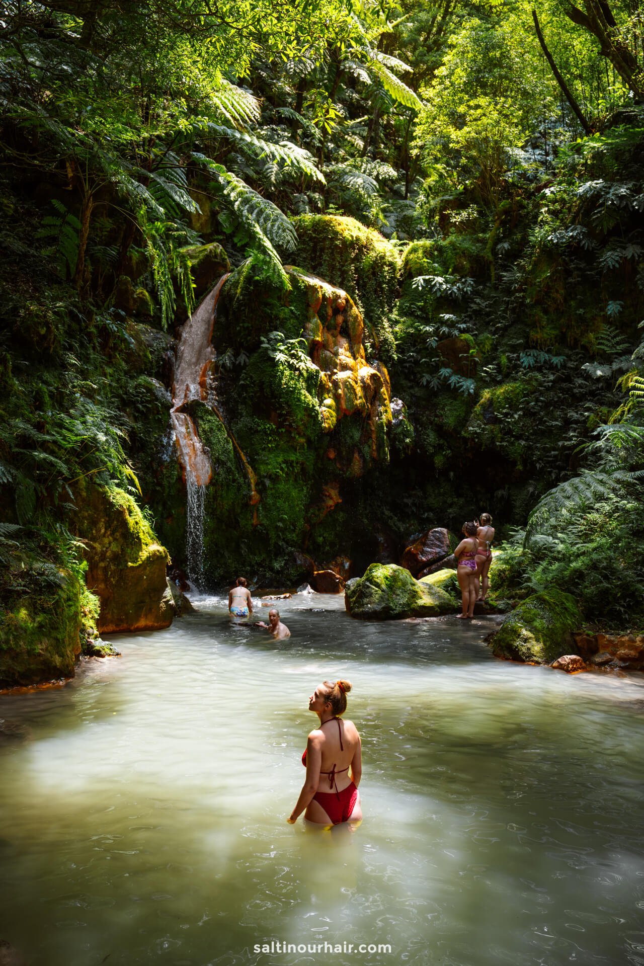 People swim and relax in a natural pool surrounded by lush greenery and a small waterfall in a forested areaâ€”one of the best things to do in SÃ£o Miguel, Azores for nature lovers.