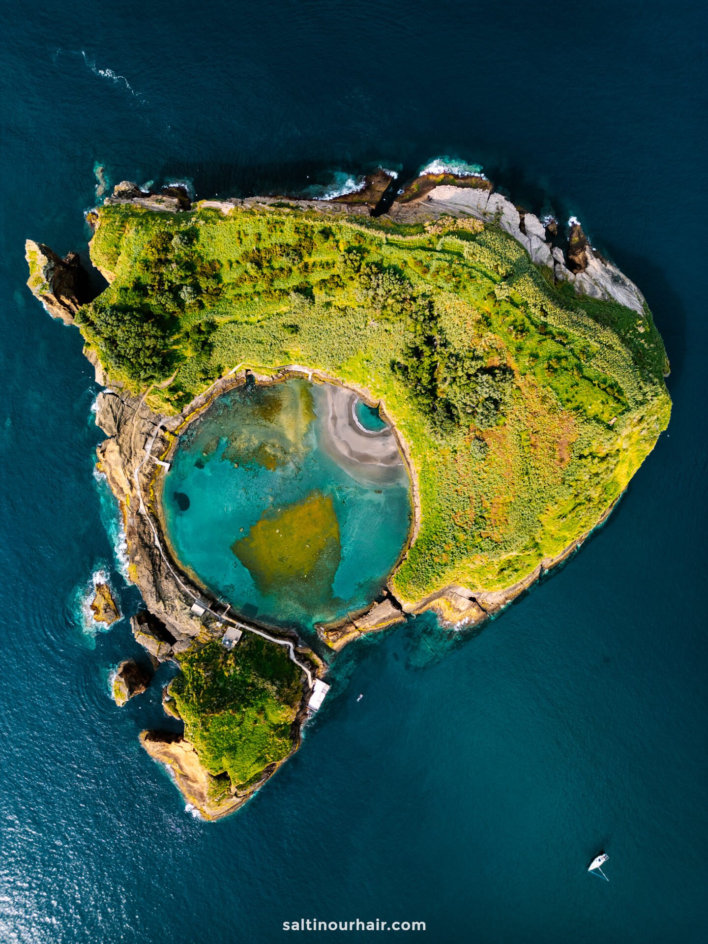 Aerial view of a small, green, heart-shaped island with a circular blue lagoon in the center, surrounded by deep blue oceanâ€”one of the remarkable sights among the things to do in SÃ£o Miguel, Azores.