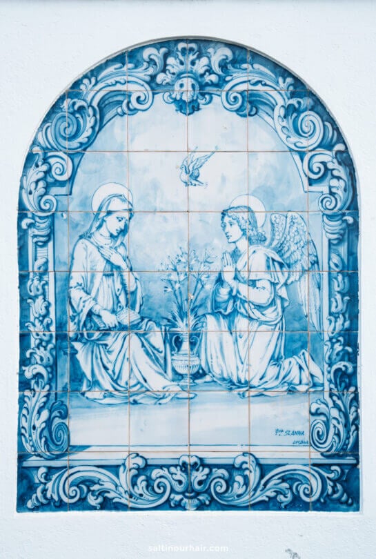Blue and white painted ceramic tiles depict the Annunciation, with the Virgin Mary and an angel kneeling in prayer, framed by ornate patternsâ€”an artistic highlight in SÃ£o Miguel.