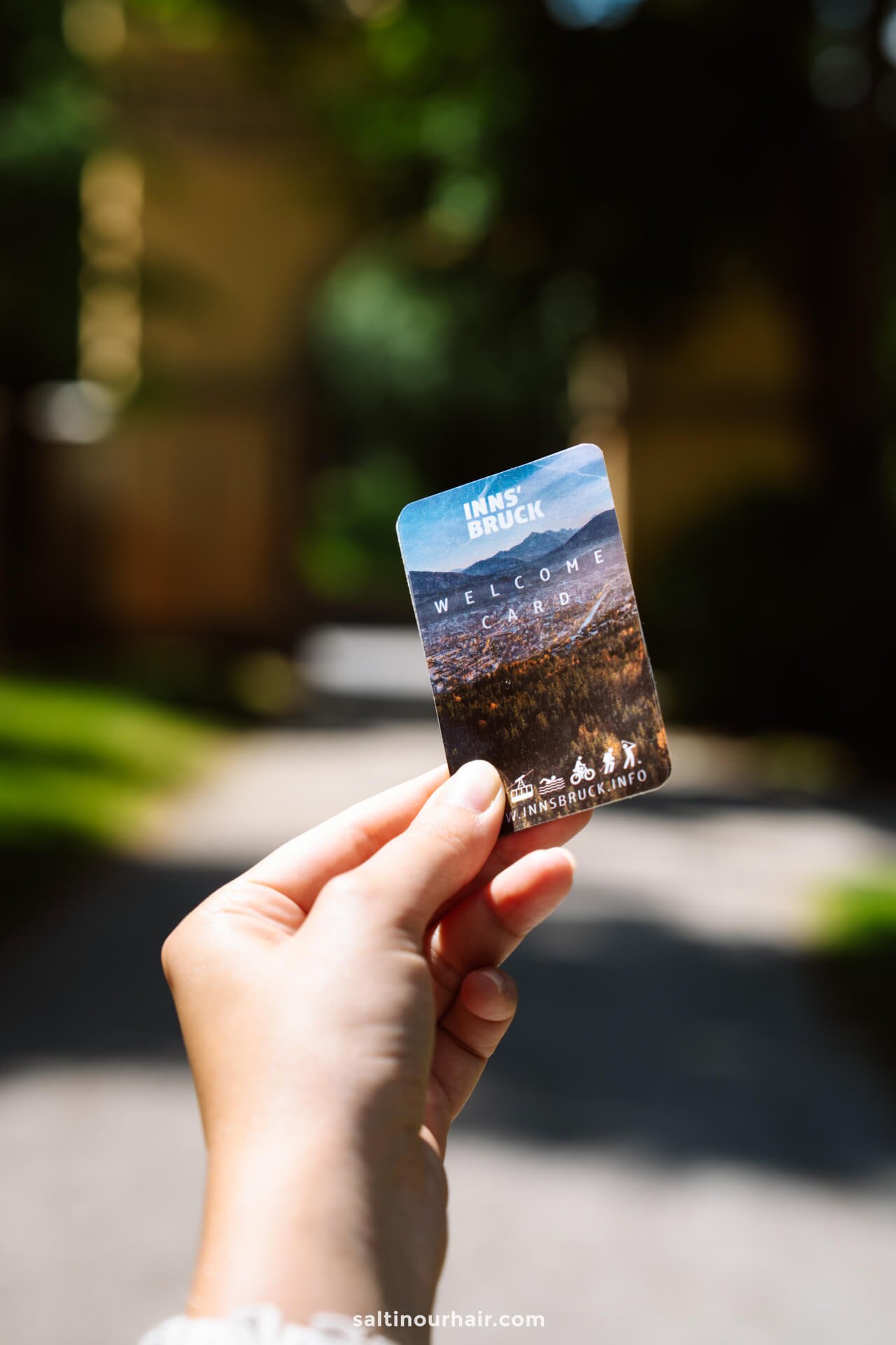 A person holds an Innsbruck Welcome Card outdoors, with a blurred green and sunlit backgroundâ€”an essential pass for exploring things to do in Innsbruck.