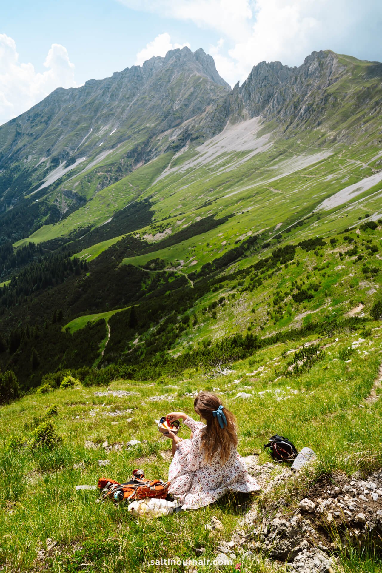 A woman with long hair sits on grass in a mountain landscape near Innsbruck, holding a camera and admiring the viewâ€”one of the memorable things to do in Innsbruck, Austria