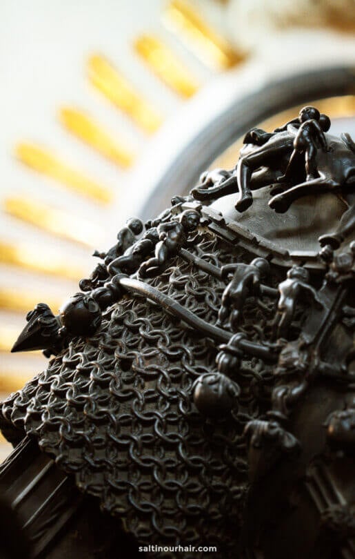 Close-up of a dark metal sculpture featuring small human figures climbing a textured, net-like surface with golden rays in the blurred backgroundâ€”one of the striking sights among the many things to do in Innsbruck.