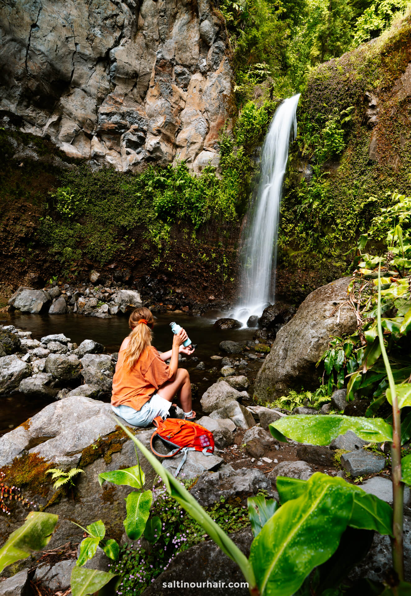 A person sits on rocks near a waterfall at Parque da grená—one of the top things to do in Furnas, sao miguel azores