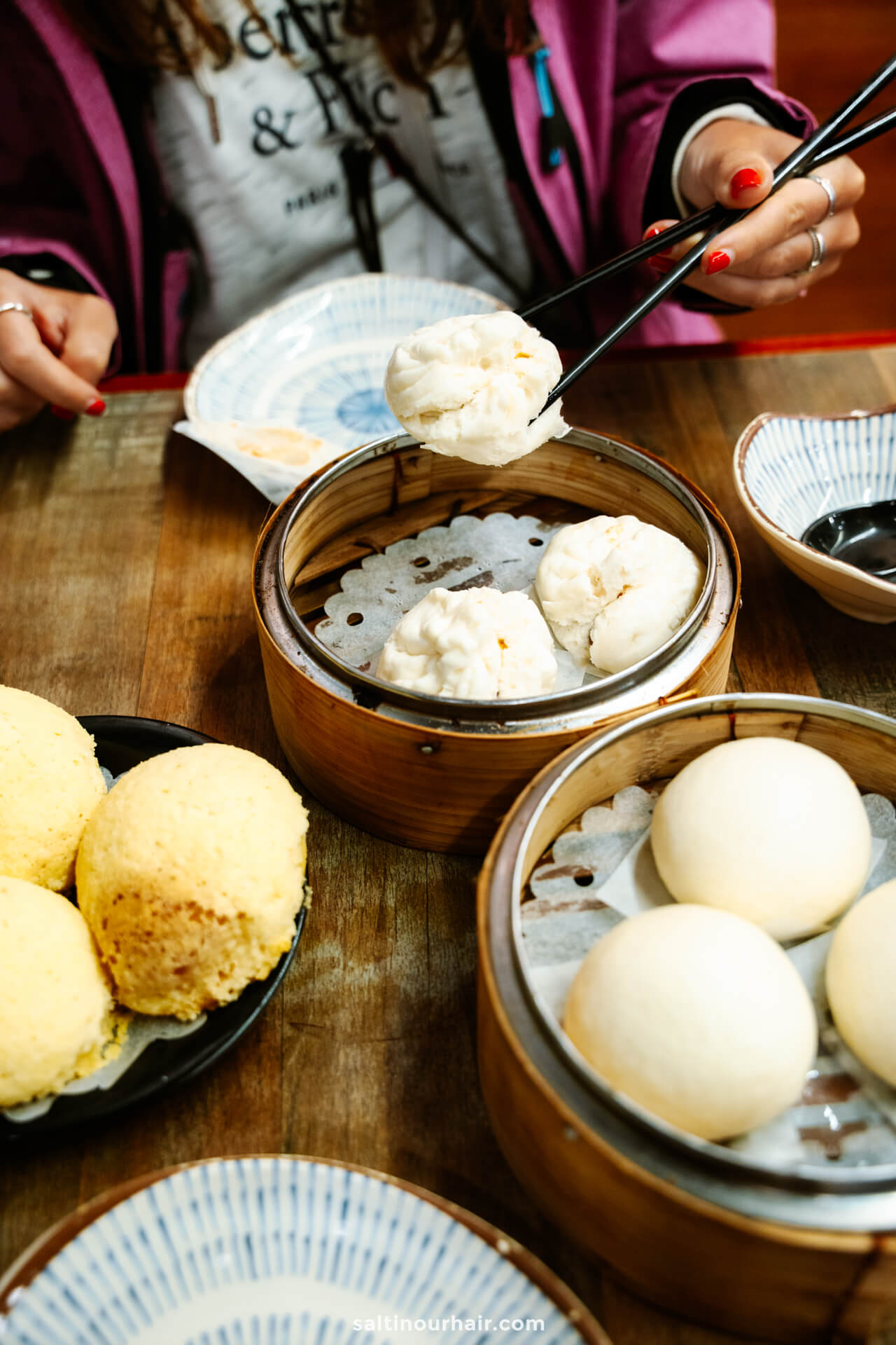 A person uses chopsticks to pick up a steamed bun from a bamboo steamer with Dim Sum