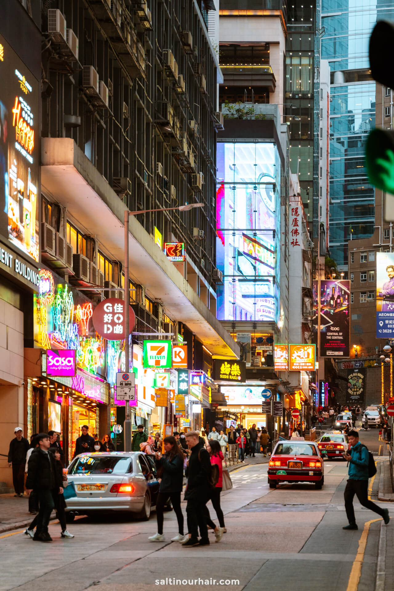 Busy city street with pedestrians crossing, cars waiting, and numerous colorful neon signs&mdash;an iconic scene to include in any Hong Kong itinerary.