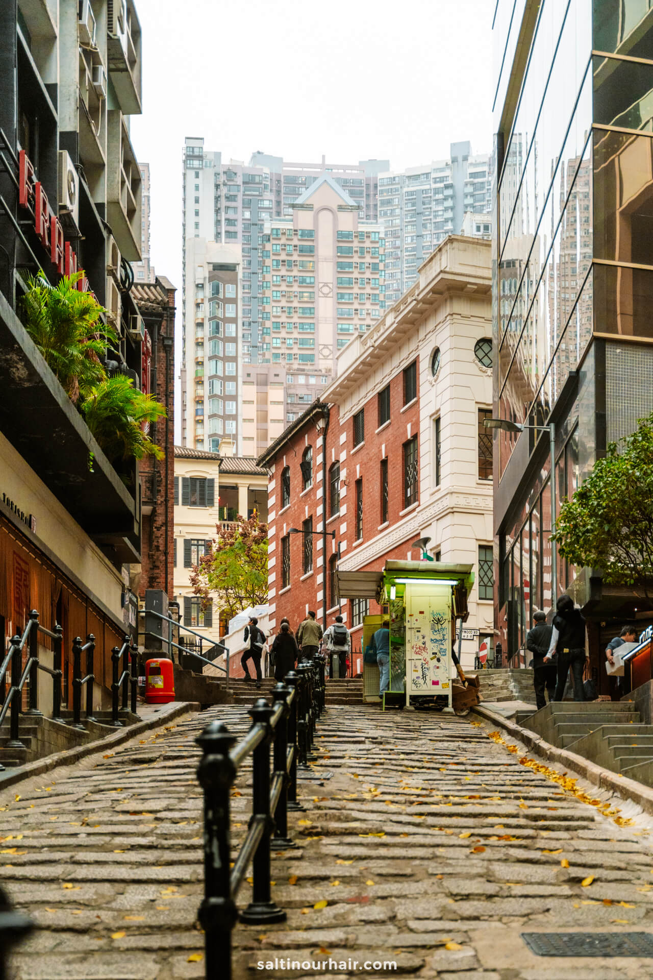 A stone-paved stair street lined with buildings, small shops, and railings, with high-rise apartments visible in the background&mdash;a must-see on any Hong Kong itinerary.