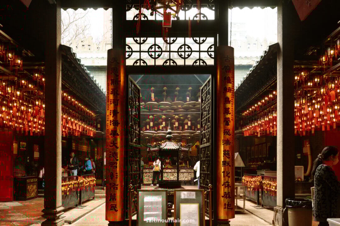 Interior of Yaumatei Tin Hau Temple in Hong Kong, with hanging red lanterns, incense coils, and a central altar beyond ornate gates