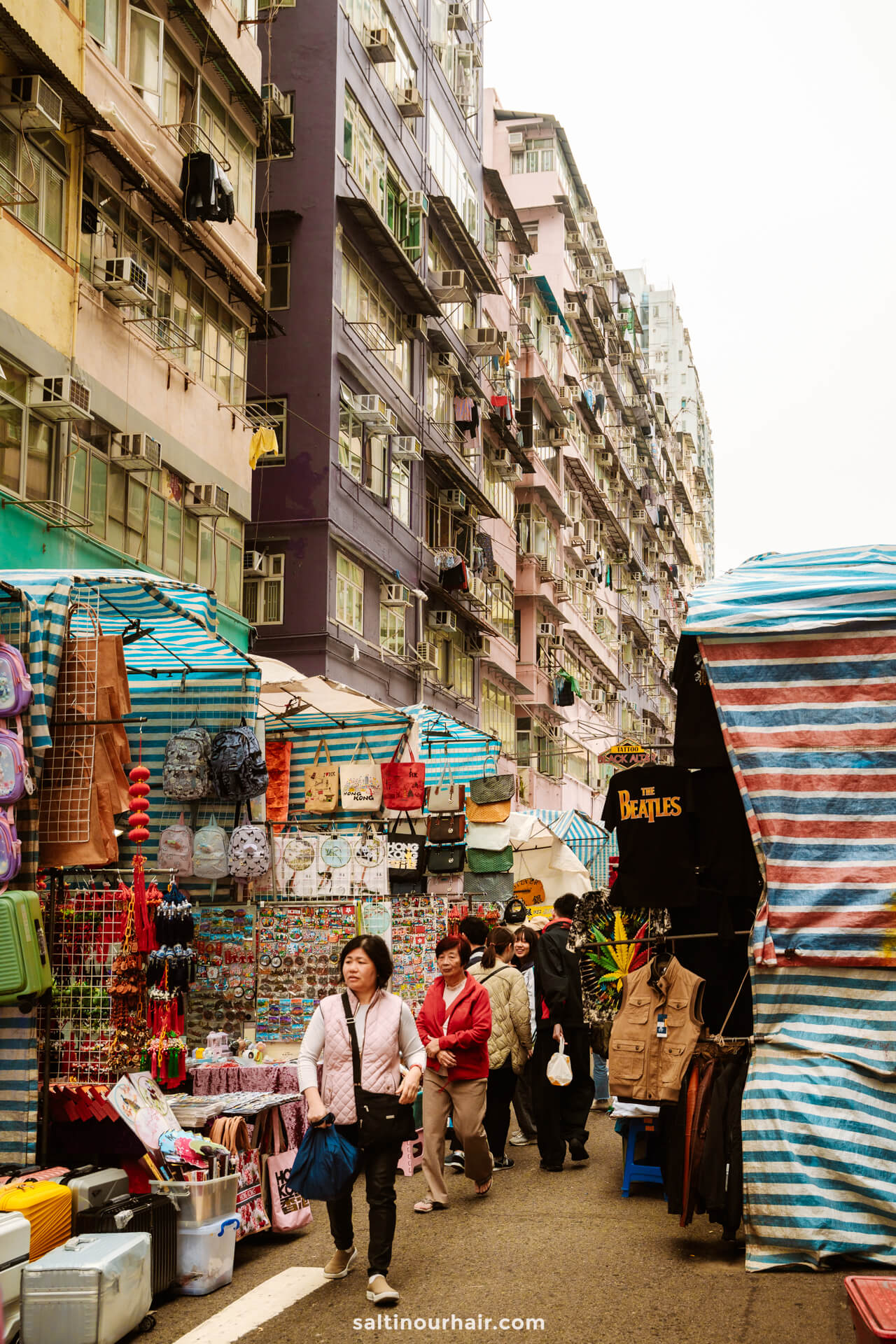 Street market in Mongkok Hong Kong with colorful stalls and shoppers, set against tall apartment buildings with balconies and hanging laundry