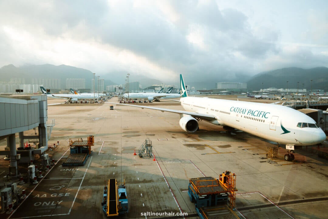 A Cathay Pacific airplane is parked at an airport gate with ground equipment nearby and several other planes in the background, offering a perfect scene for any hong kong itinerary.