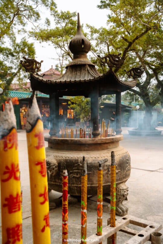 Large stone incense burner with many burning incense sticks, surrounded by tall colorful incense poles at an outdoor temple in Lantau Island, Hong Kong
