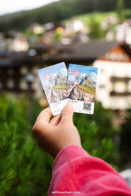 A hand holds two scenic mountain cable car tickets to go up to the Seceda —one of the must-try things to do in the Dolomites.