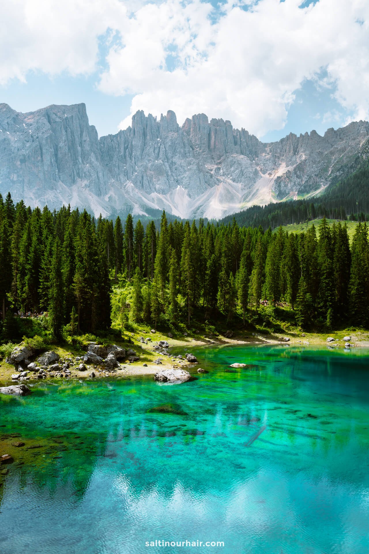 Clear turquoise lake called lago di carezza surrounded by pine trees and rocky mountains under a partly cloudy sky—a perfect spot to add to your list of things to do in the Dolomites.