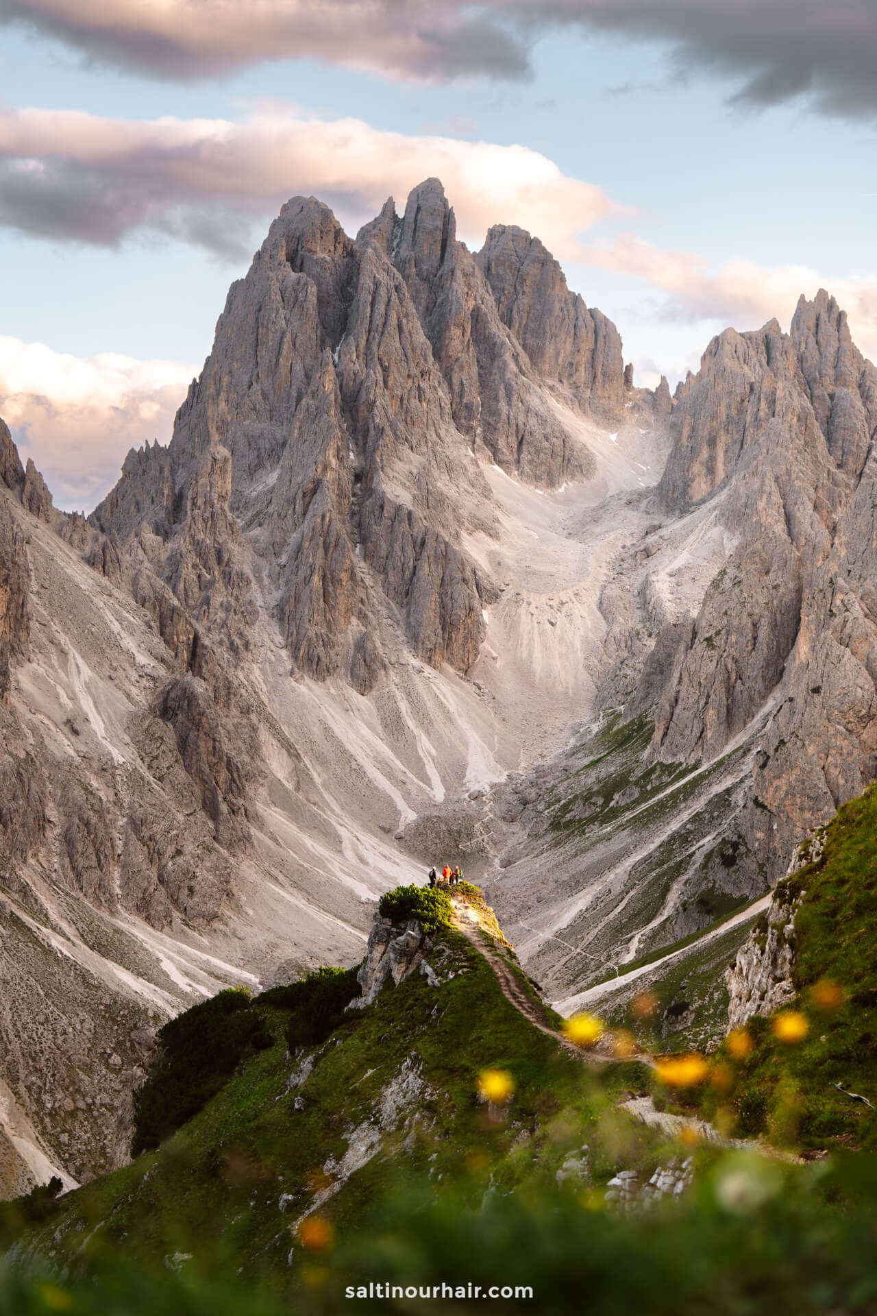 A group of people stands on a grassy ridge in the Dolomites, with dramatic rocky mountains in the background under a partly cloudy sky—Cadini di Misurina is one of the top things to do in the Dolomites for breathtaking views.