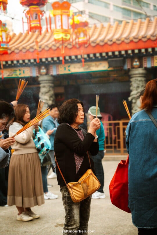 People hold and burn incense sticks while praying at an outdoor temple, with decorative lanterns and traditional architecture in the background&mdash;a peaceful highlight on any Hong Kong itinerary.