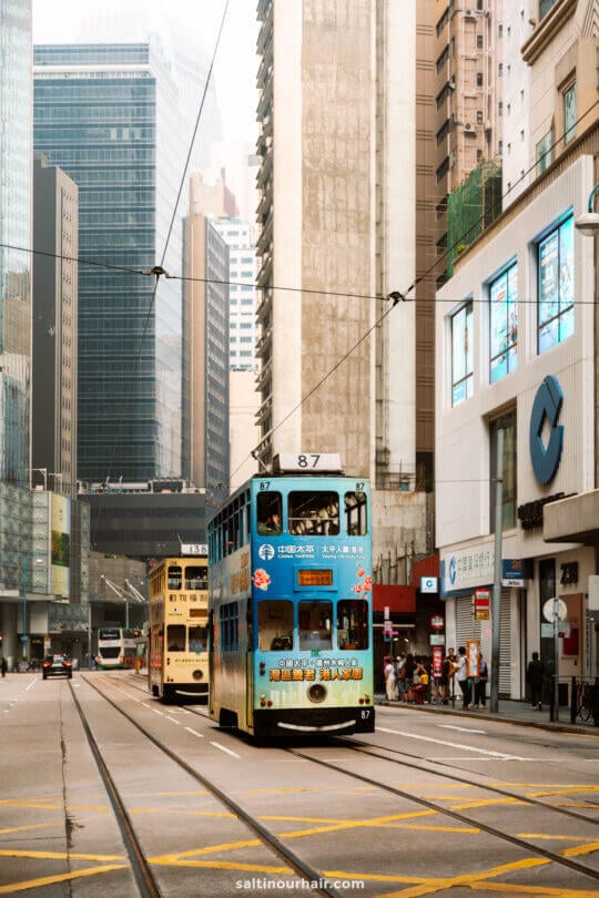 Double-decker trams travel along tracks in Hong Kong lined with tall buildings