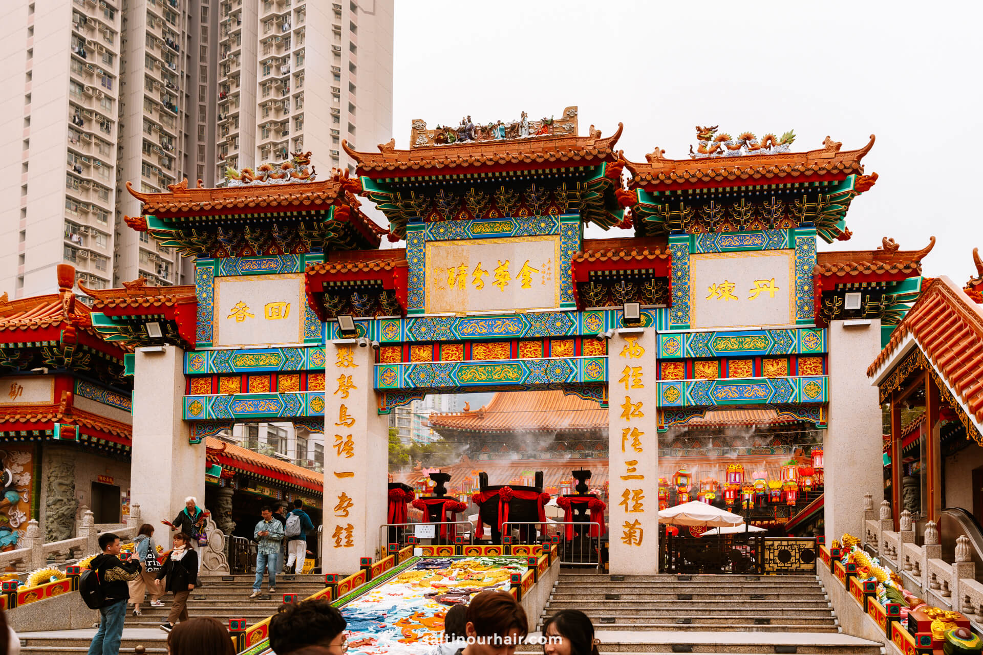 Sik Sik Yuen Wong Tai Sin Temple entrance with intricate decorations, incense smoke, and people gathered in front&mdash;an essential stop on any Hong Kong itinerary&mdash;with modern high-rise buildings visible in the background.