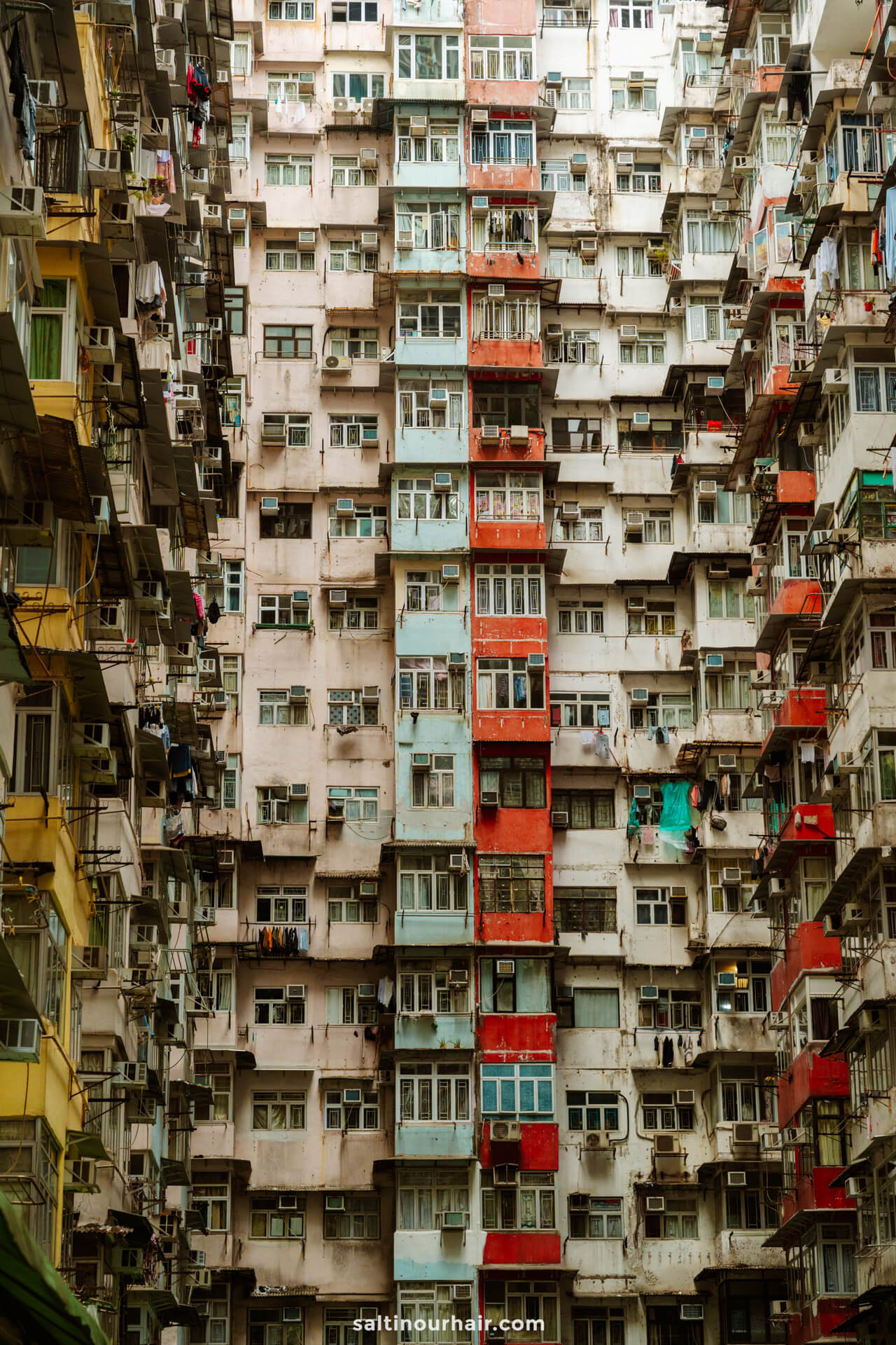 High-rise apartment building with crowded balconies, window air conditioners, and laundry hanging outside&mdash;a familiar sight on any Hong Kong itinerary. The weathered facade is densely packed, capturing the city&rsquo;s vibrant urban energy.