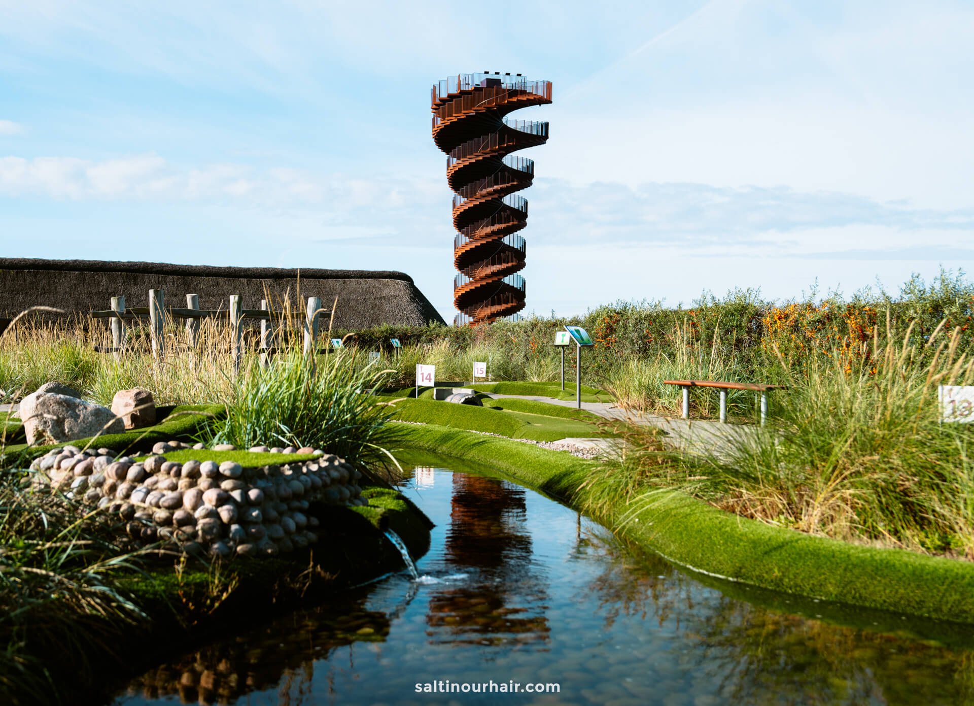 A highlight for any Denmark itinerary, this spiral observation Marsk Tower rises above landscaped gardens with a winding stream, benches, and educational signs under a clear sky.