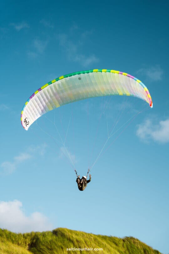 A person paraglides above grassy hills under a clear blue sky, capturing the adventurous spirit of any Denmark itinerary.