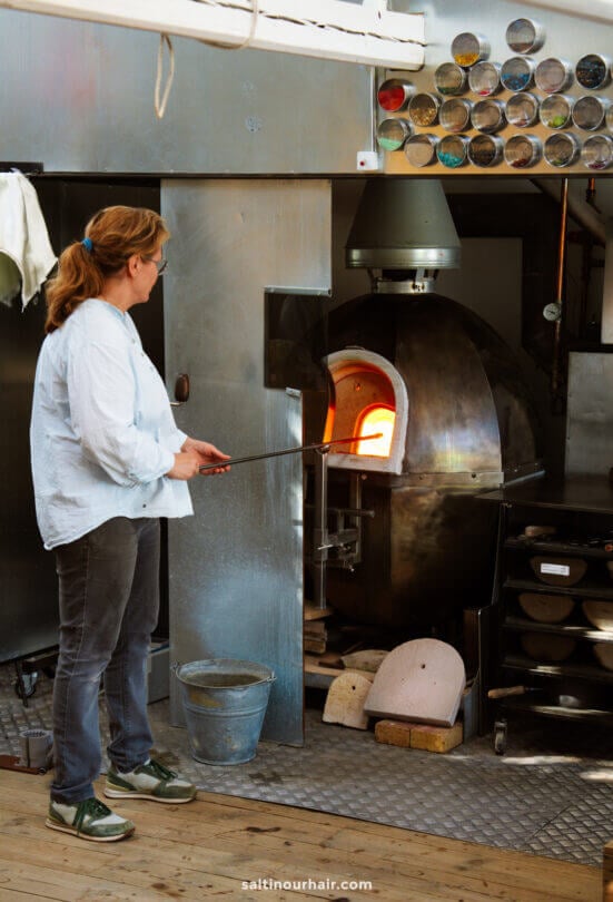 A person stands in front of a glassblowing furnace in Denmark, holding a metal rod with molten glass—an unforgettable experience to add to any Denmark itinerary.